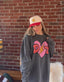 Person in a star cap with braided hair wears an oversized sweatshirt with a pink heart and “DC” on it, standing in front of a brick wall and a bench with a cozy cushion and blanket.