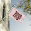 The Disco Tribe Flag features the words DISCO TRIBE in bold, retro brown letters with orange star-like accents on a pink background and is displayed waving on a flagpole outside near a white building and green trees.