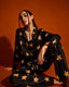 A woman wearing a black and gold pajama top with star patterns is sitting on the floor against an orange background.