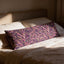 A decorative pillow with a floral pattern rests on a bed, bathed in soft sunlight streaming through a window.