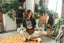 Wearing the Epic Playlist Society Crop Top, a woman sits cross-legged on an orange patterned rug, laughing. She is reflected in a large mirror surrounded by plants and disco balls, creating vibrant festival outfit vibes.