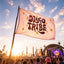 A vibrant Festival Flag, Totem Flag for Camping & Music Festivals, Boho Tapestry Flag, Music Festival Decor featuring the words “DISCO TRIBE” and orange stars waves at a lively event. The backdrop of the stage and lights, along with a crowd under a clear blue sky, beautifully captures the electrifying atmosphere of an EDM celebration with this striking festival decor in action.
