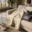 a pair of beige sweatpants with a lightning bolt design, a black hoodie with the text "DREAM WORLDWIDE" printed on it, and a pair of white sneakers placed on a beige couch.
