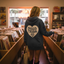 A woman browsing through vinyl records in a record store, wearing a blue hoodie with the text "DISCO TRIBE CO" printed on it.