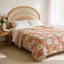 a bedroom with a bed featuring a floral bedspread and a wooden headboard. There is a nightstand next to the bed with a vase of flowers and an open book.